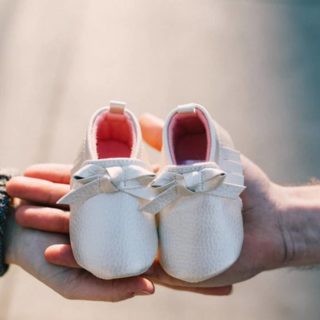 two hands holding a pair of baby shoes